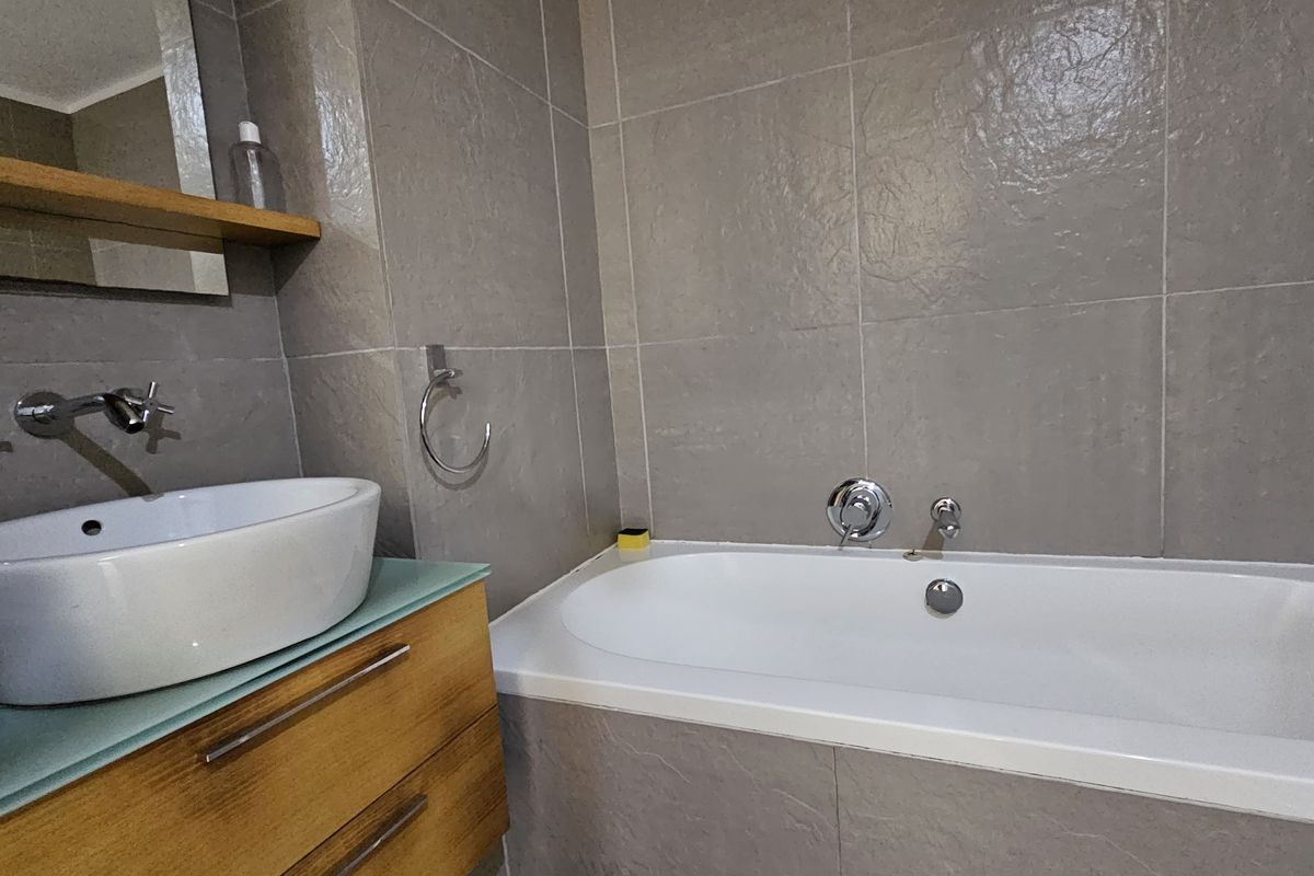 Modern bathroom featuring a vessel sink on a floating vanity, wall-mounted fixtures, and a tiled built-in bathtub.