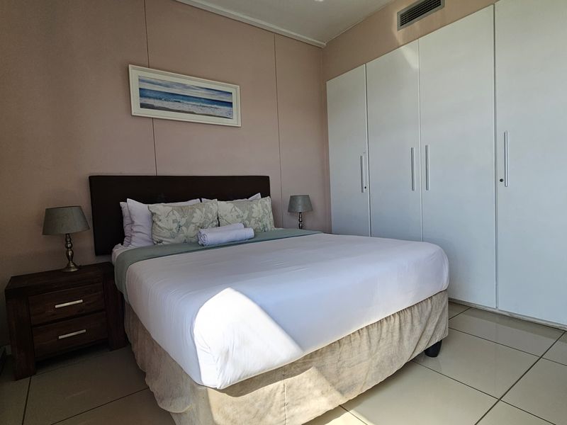 A well-maintained bedroom featuring neutral walls, large built-in cupboards, tiled flooring, and integrated ducted air conditioning.