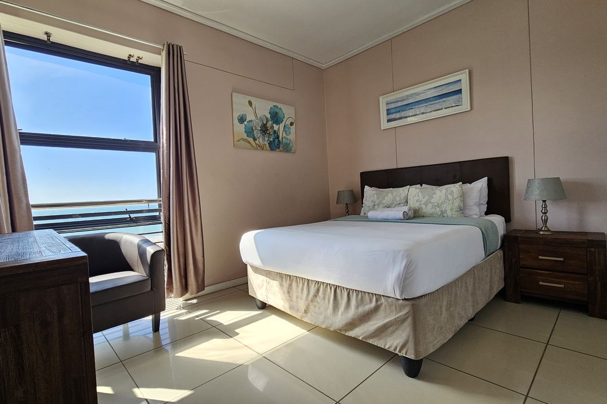 A well-lit bedroom featuring tiled flooring and a large window with ocean views, providing a bright and comfortable living space.