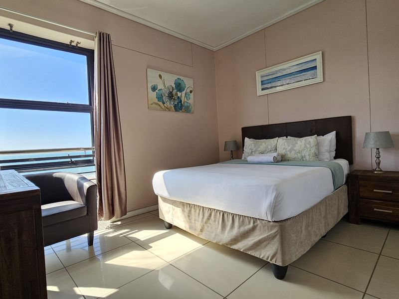 A well-lit bedroom featuring tiled flooring and a large window with ocean views, providing a bright and comfortable living space.