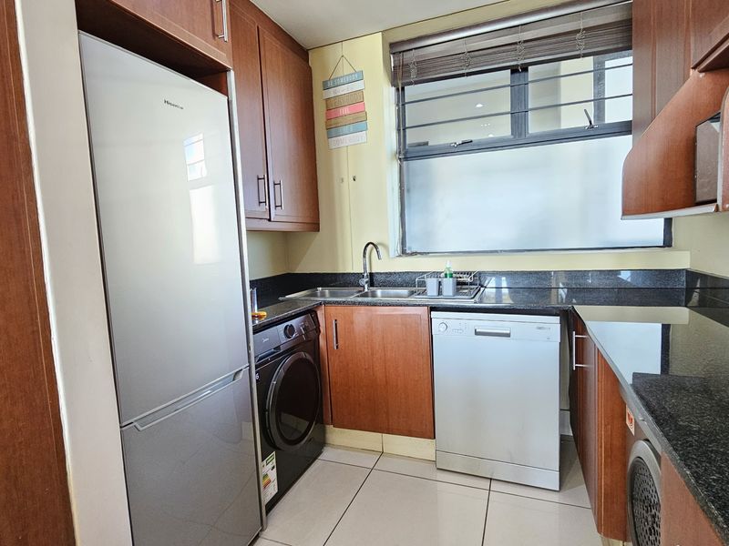 A functional kitchen featuring granite countertops, wooden cabinetry, tiled flooring, and a window with security bars, providing a practical workspace.