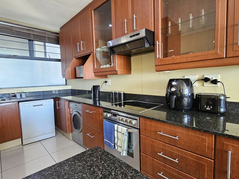 A functional kitchen featuring dark granite countertops, warm-toned wooden cabinetry, integrated appliances, and tiled flooring with ample storage space.