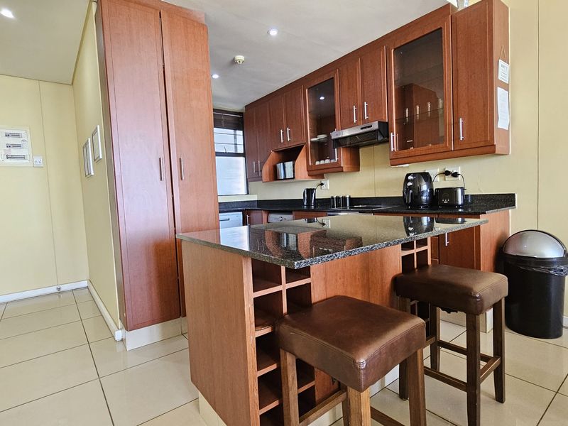A functional kitchen featuring wood-finish cabinetry, granite countertops, a breakfast nook with integrated wine storage, and tiled flooring.