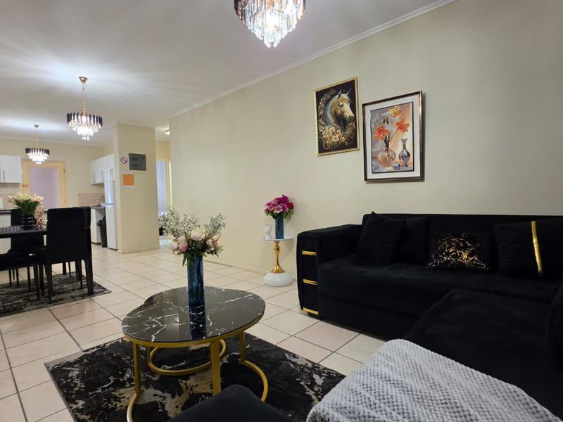 An open-plan living and dining area featuring tiled flooring, modern kitchen cabinetry, and elegant crystal chandeliers, creating a cohesive and functional living space.