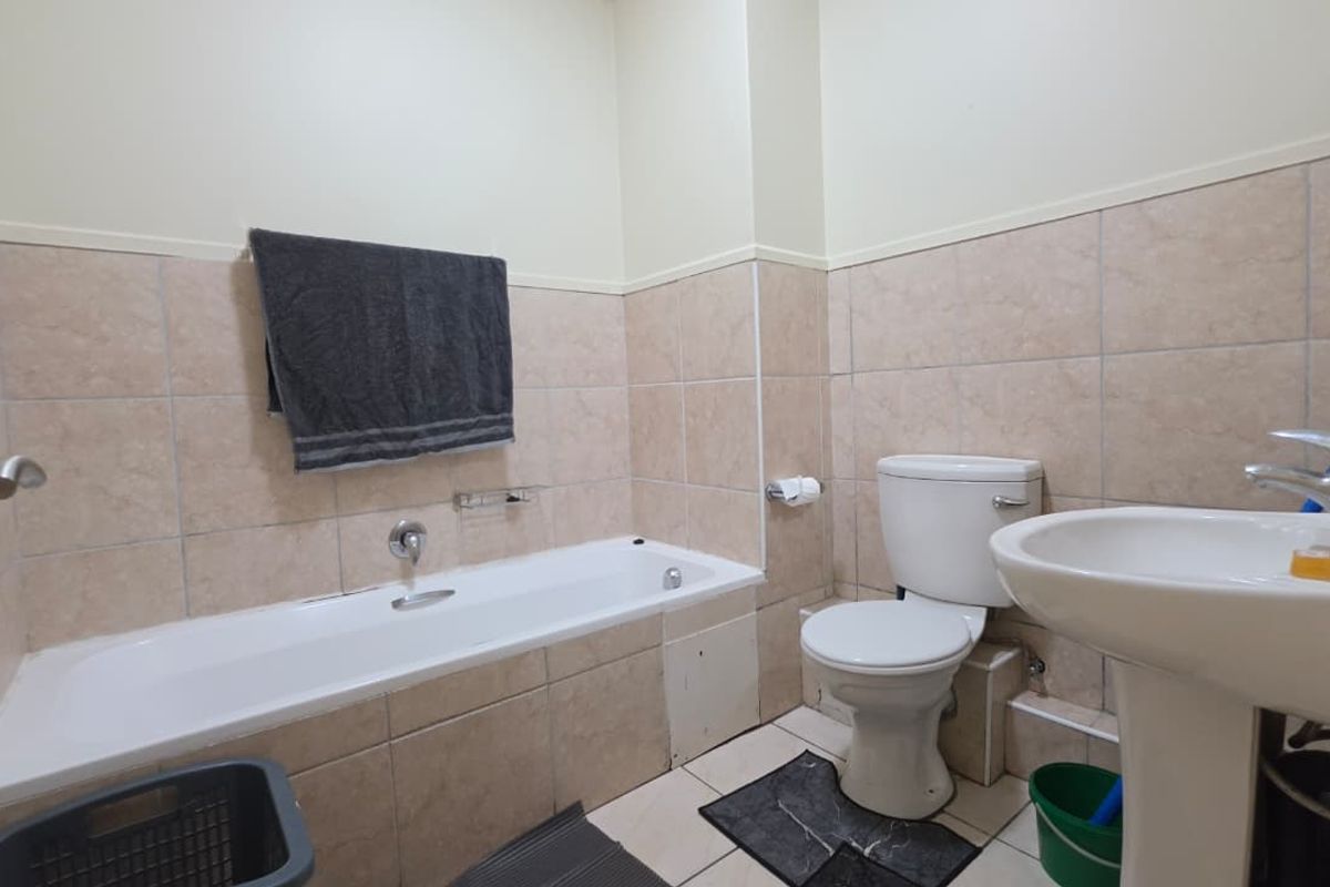 A functional bathroom featuring a bathtub, pedestal basin, and toilet with neutral ceramic wall and floor tiling.