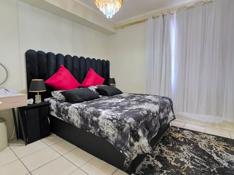A well-lit bedroom featuring tiled flooring and a decorative crystal chandelier, providing a functional and comfortable sleeping space.