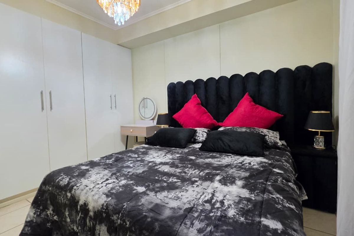 A well-maintained bedroom featuring floor-to-ceiling built-in cupboards, tiled flooring, and a decorative chandelier.