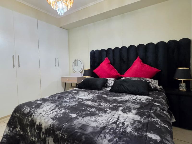 A well-maintained bedroom featuring floor-to-ceiling built-in cupboards, tiled flooring, and a decorative chandelier.