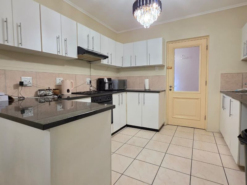 A functional kitchen featuring white cabinetry, dark granite countertops, tiled flooring, and a glass-paneled door leading to an exterior area.