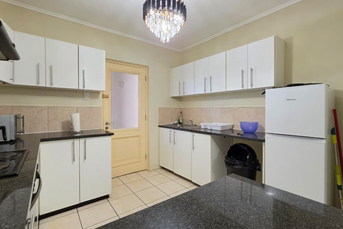 A functional kitchen featuring white cabinetry, dark granite countertops, tiled backsplash, and ceramic flooring, providing a clean and practical workspace.