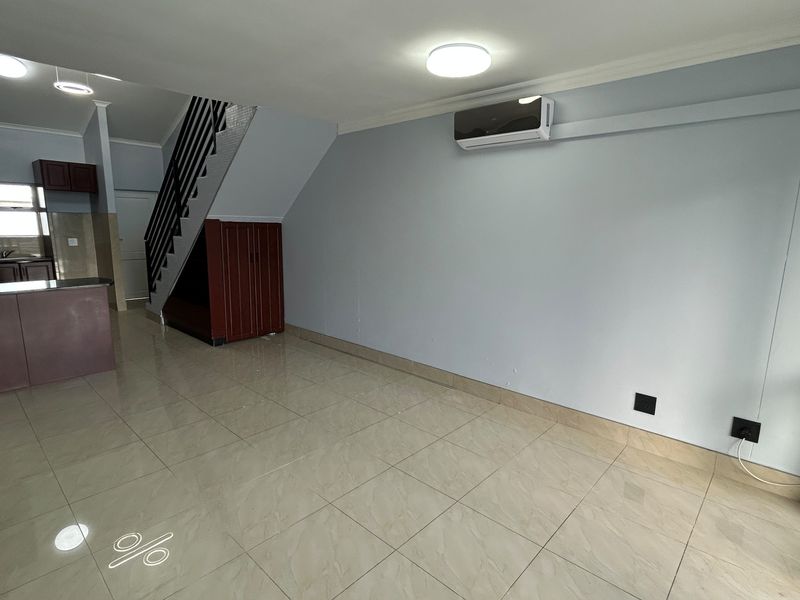 Open-plan living area featuring tiled flooring, a split-system air conditioner, and an integrated kitchen space with a staircase.