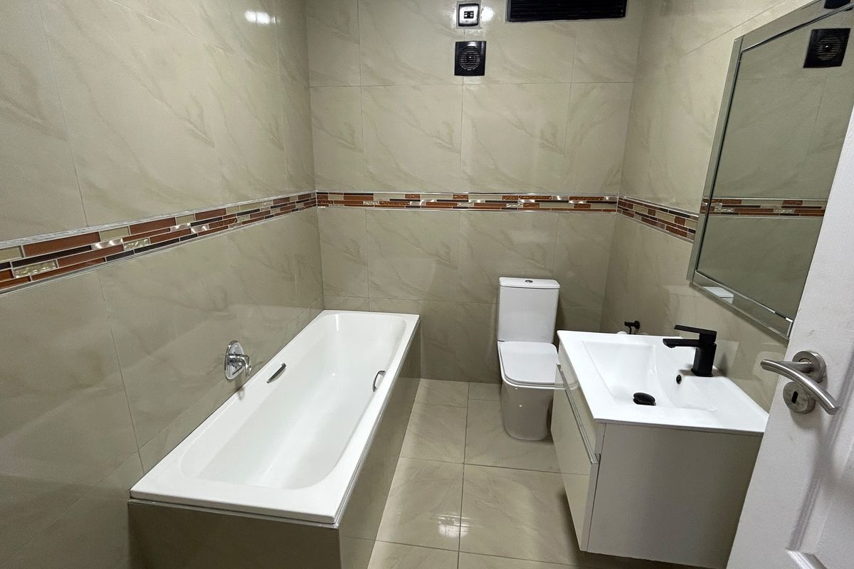 A modern, well-maintained bathroom featuring a bathtub, a sleek vanity with a basin, and neutral wall tiling with a decorative accent border.