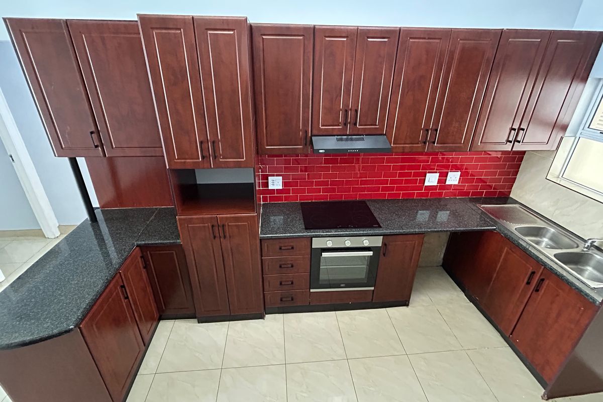 A clean, functional kitchen featuring dark wood cabinetry, granite countertops, a striking red subway tile backsplash, and integrated cooking appliances.
