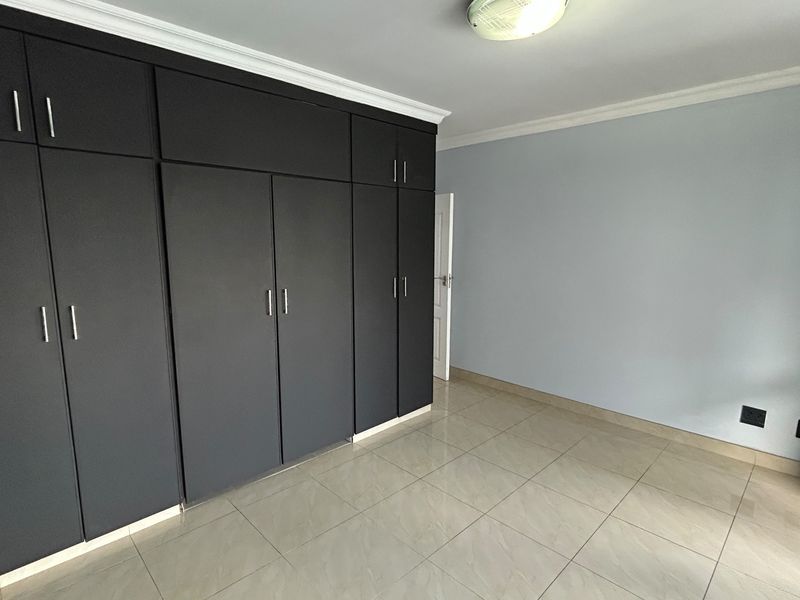 A bright, empty bedroom featuring modern dark built-in cupboards, neutral tiled flooring, and clean wall finishes.