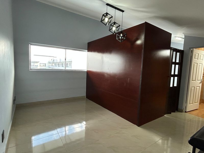 An empty living area featuring polished tiled flooring, a central partition wall, and modern pendant lighting, with an adjacent bathroom visible.