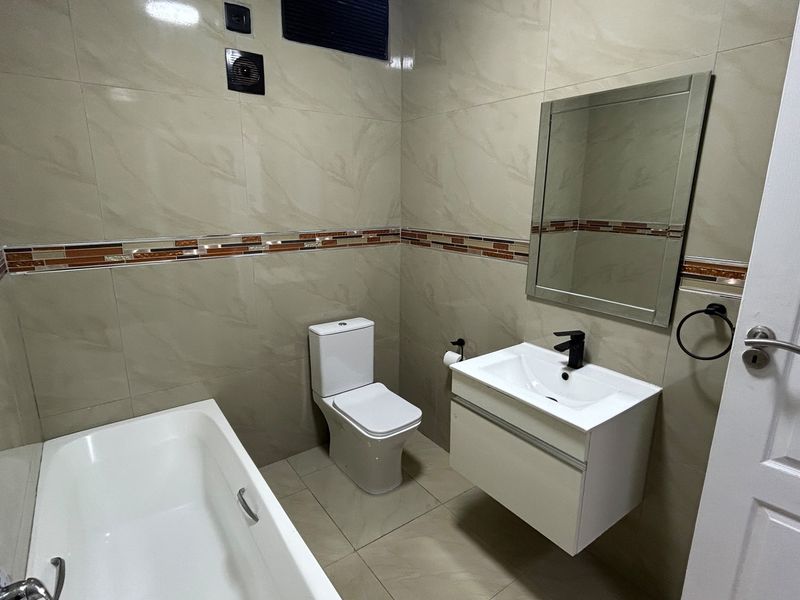 A modern bathroom featuring a wall-mounted vanity, bathtub, toilet, and neutral tiled finishes throughout.