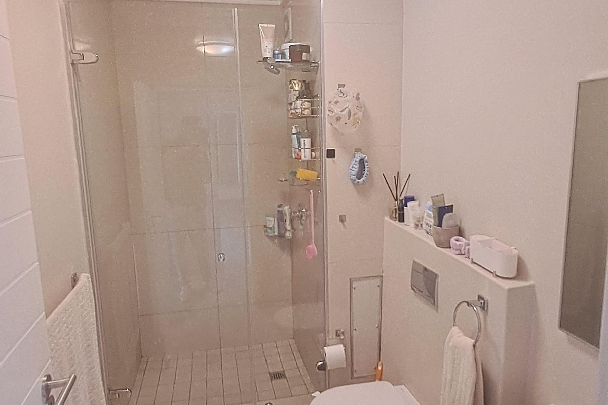 A compact, modern bathroom featuring a glass-enclosed shower, wall-mounted toilet with integrated flush plate, and a vanity basin with neutral tiling throughout.