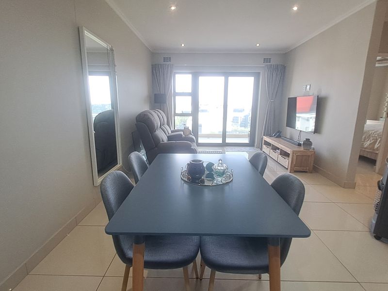 An open-plan living and dining area featuring neutral tiled flooring, recessed downlighting, and a large sliding glass door leading to a balcony.