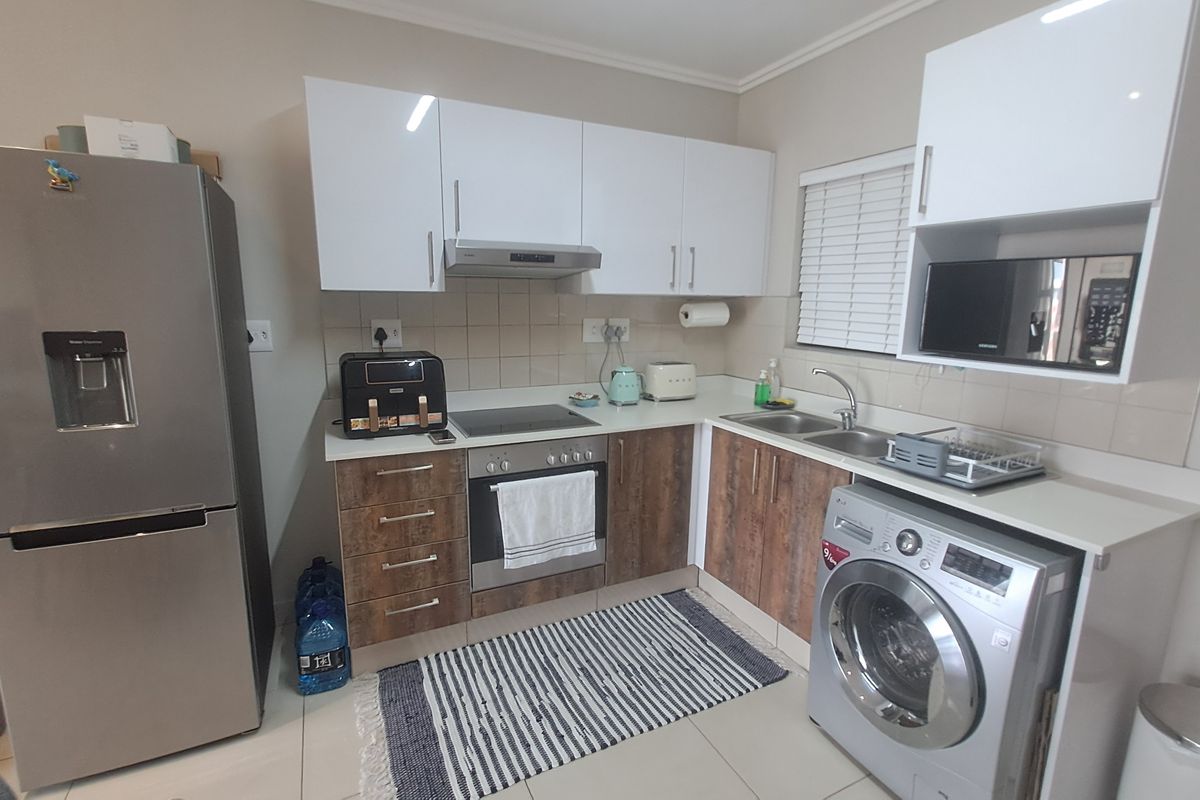 Modern kitchen featuring white upper cabinets, wood-finish lower cabinetry, integrated appliances, stainless steel sink, and tiled backsplash.