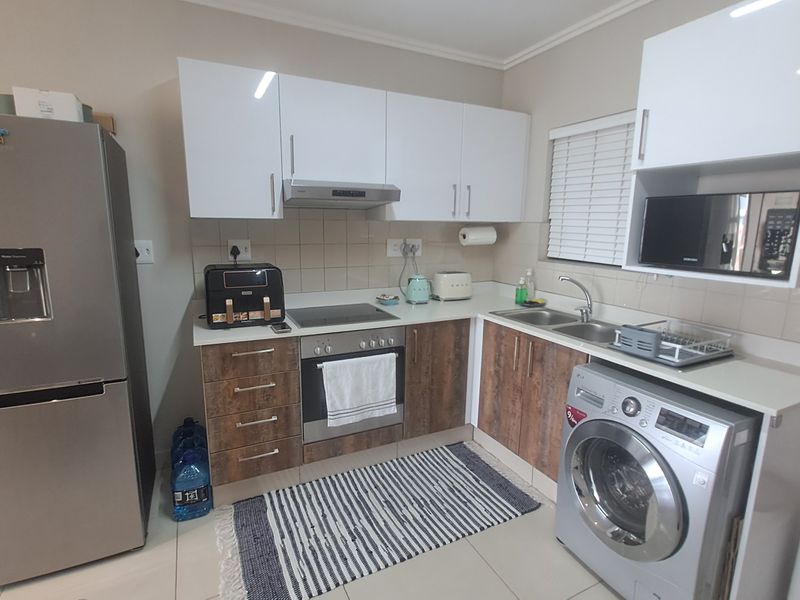 Modern kitchen featuring white upper cabinets, wood-finish lower cabinetry, integrated appliances, stainless steel sink, and tiled backsplash.