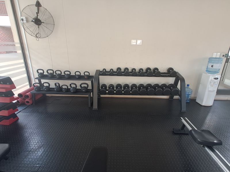 A functional gym space featuring durable rubberized flooring, a wall-mounted industrial fan, and access through a glass door.