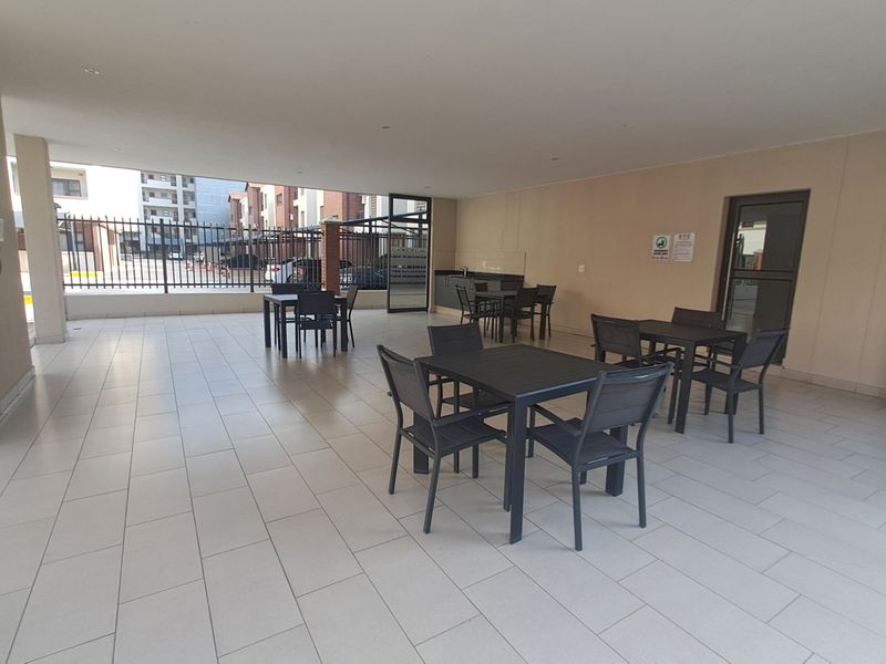 A spacious covered outdoor patio area featuring tiled flooring, recessed lighting, and a small built-in kitchenette counter, suitable for communal or private outdoor entertainment.