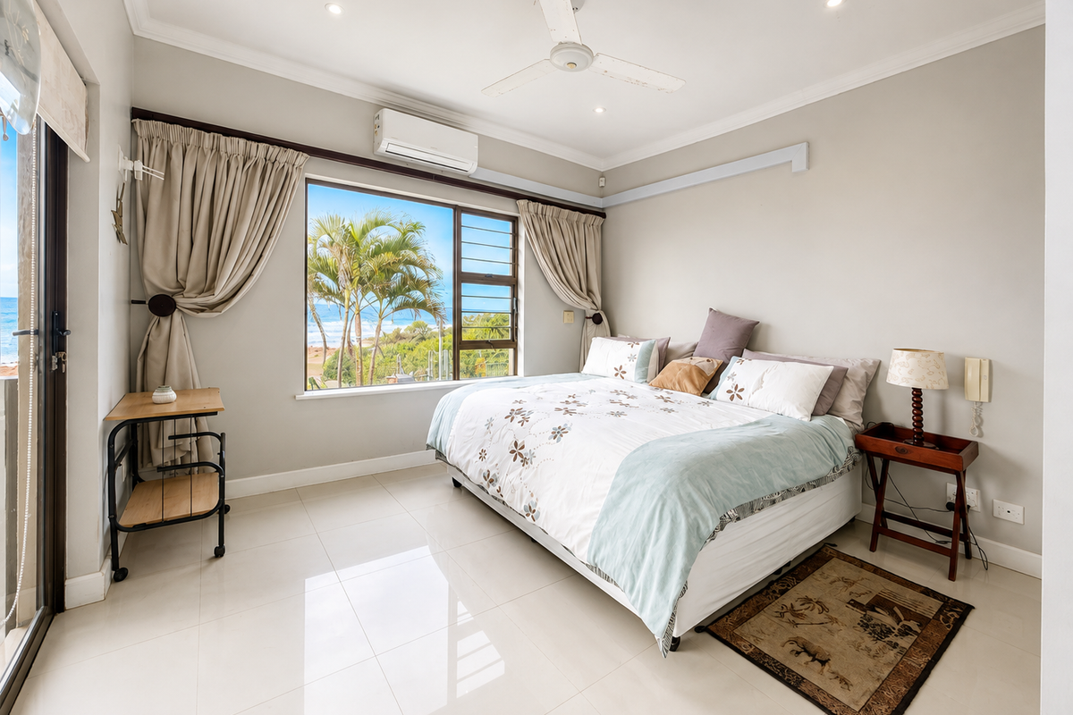 A bright and spacious bedroom featuring tiled floors, a ceiling fan, air conditioning, and a large window with scenic coastal views.