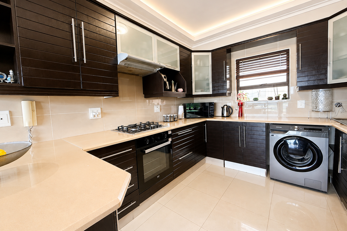 Modern kitchen featuring dark wood cabinetry, stone countertops, built-in gas hob, oven, and integrated washing machine with neutral tiled flooring.