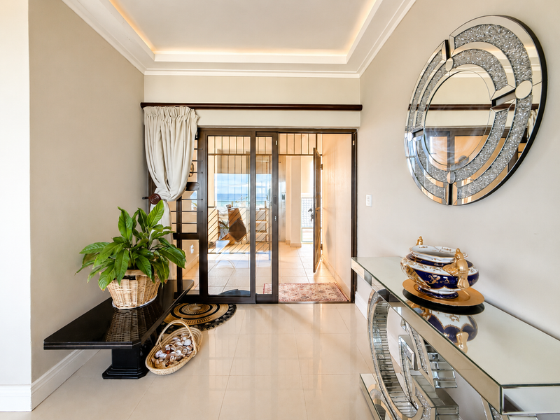 A bright, well-maintained hallway featuring tiled flooring, recessed cove lighting, and a sliding glass door leading to an outdoor balcony area.