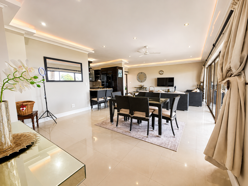 Spacious open-plan living and dining area featuring polished porcelain tiles, recessed cove lighting, and large sliding glass doors leading to an outdoor space.