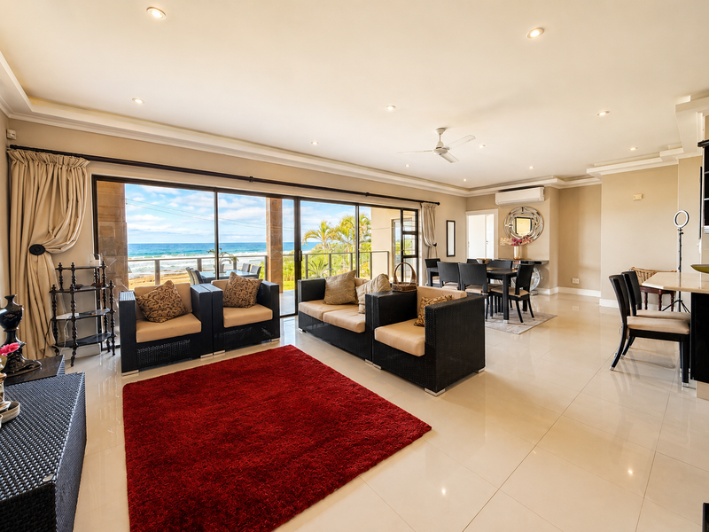 Spacious open-plan living and dining area featuring large sliding glass doors that open to a balcony with ocean views and modern tiled flooring.