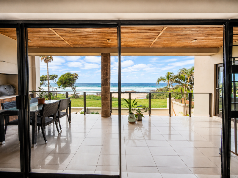 Spacious covered patio featuring tiled flooring, a timber slat ceiling, and a built-in braai, offering direct access and expansive ocean views.