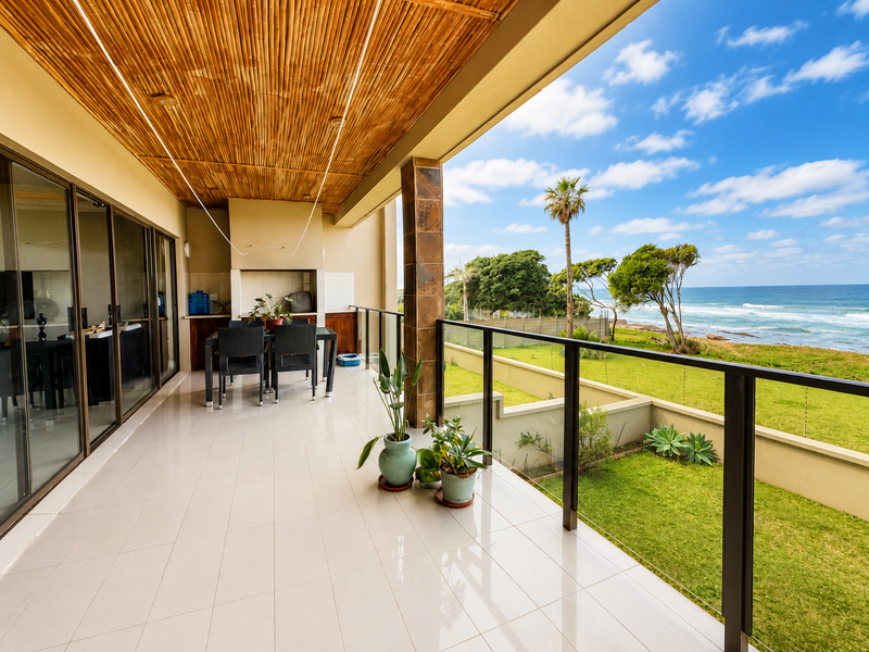 Spacious covered balcony featuring a bamboo ceiling, built-in braai, and glass balustrade, offering expansive ocean views and direct access to the living area.