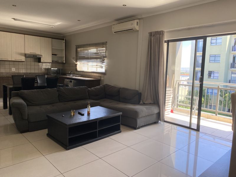 Open-plan living area featuring tiled floors, a functional kitchen with built-in cabinetry, and direct access to a private balcony through sliding glass doors.
