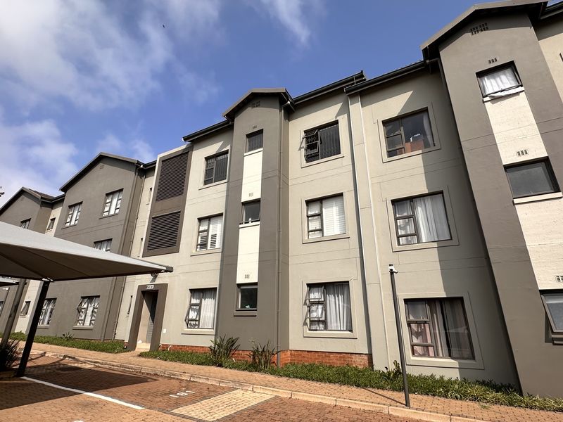 Exterior view of a modern multi-story apartment complex featuring paved parking areas, covered carports, and well-maintained facade finishes.
