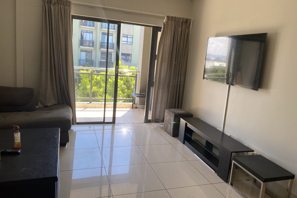 A bright living room featuring large format floor tiles and a sliding glass door providing direct access to a private balcony.