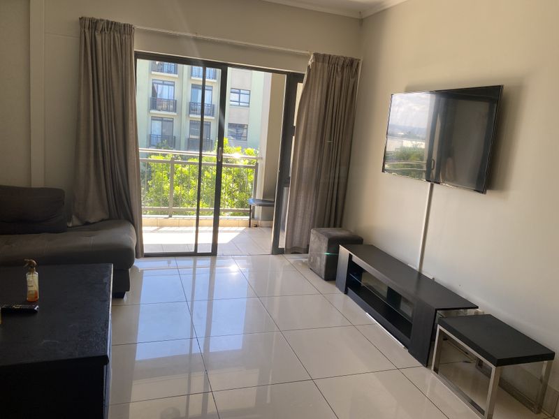A bright living room featuring large format floor tiles and a sliding glass door providing direct access to a private balcony.