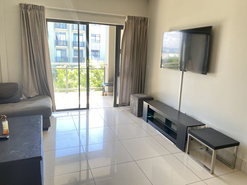 A bright living room featuring large format floor tiles and a sliding glass door that opens onto a private balcony.