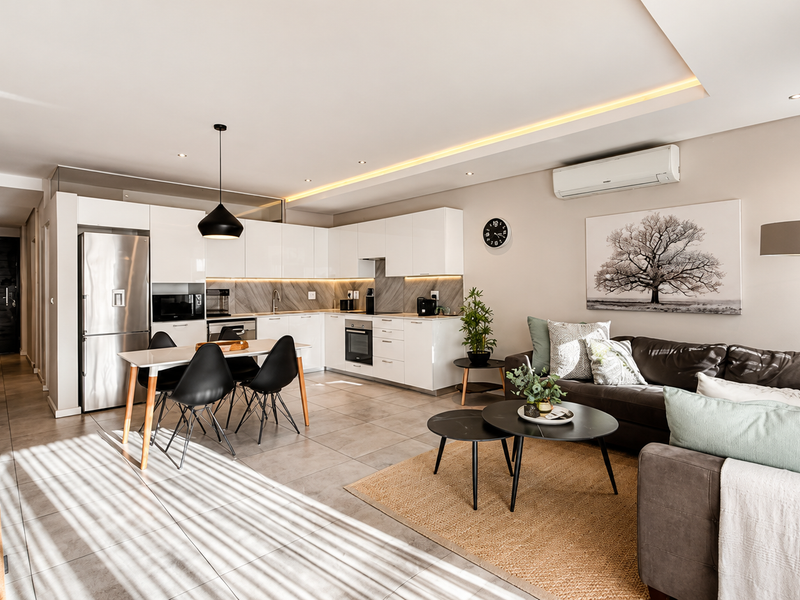 Modern open-plan living area featuring a sleek kitchen with built-in appliances, recessed lighting, and tiled flooring, seamlessly flowing into a comfortable lounge space.