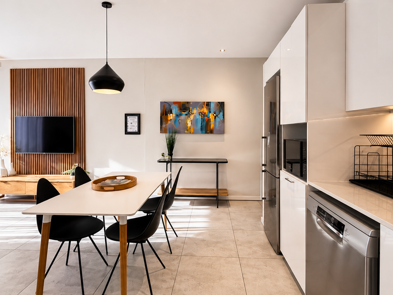 Modern open-plan living and kitchen area featuring sleek white cabinetry, stone countertops, integrated appliances, and a stylish slatted wood feature wall.