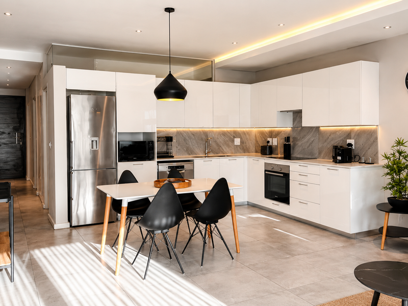 Modern open-plan kitchen and dining area featuring sleek white cabinetry, stone backsplash, integrated appliances, and contemporary recessed lighting.