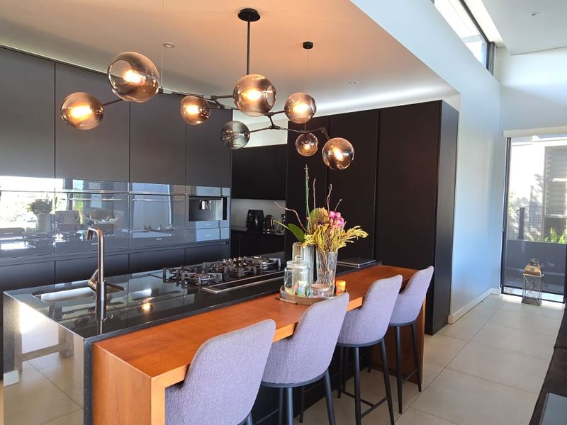 Modern open-plan living area featuring a sleek kitchen with dark cabinetry, a large island with gas cooktop, and stylish timber wall accents.