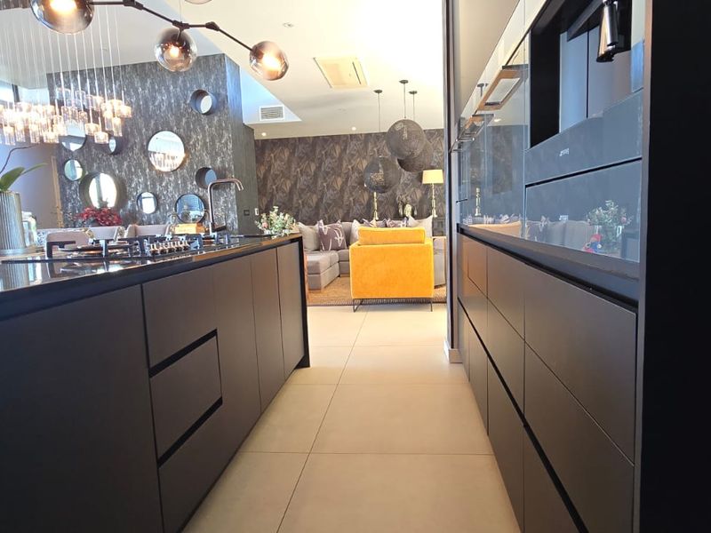 Modern open-plan kitchen featuring sleek dark cabinetry, a central island with a gas hob, and integrated appliances, flowing into the living area.
