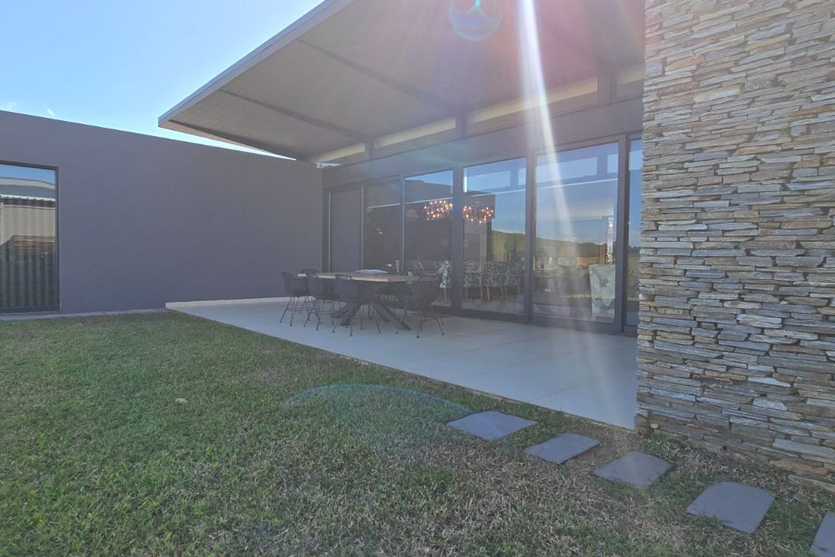 A modern rear exterior view featuring a covered patio, stone-clad wall, and large sliding glass doors opening onto a well-maintained garden.