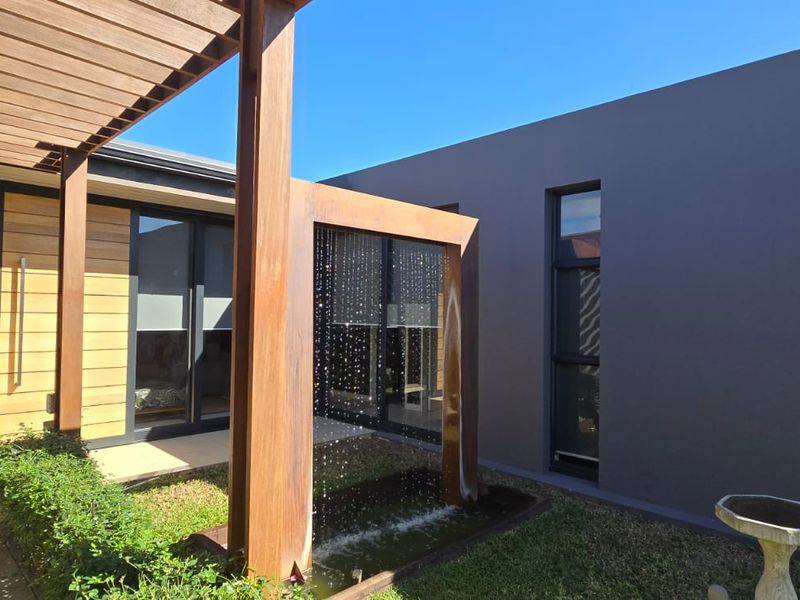 Modern outdoor patio area featuring a timber pergola, a contemporary water feature, and seamless access to the interior living space.