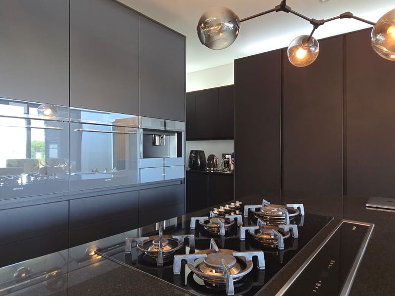 Modern kitchen featuring sleek dark cabinetry, integrated high-end appliances, a central island with a gas cooktop, and contemporary pendant lighting.