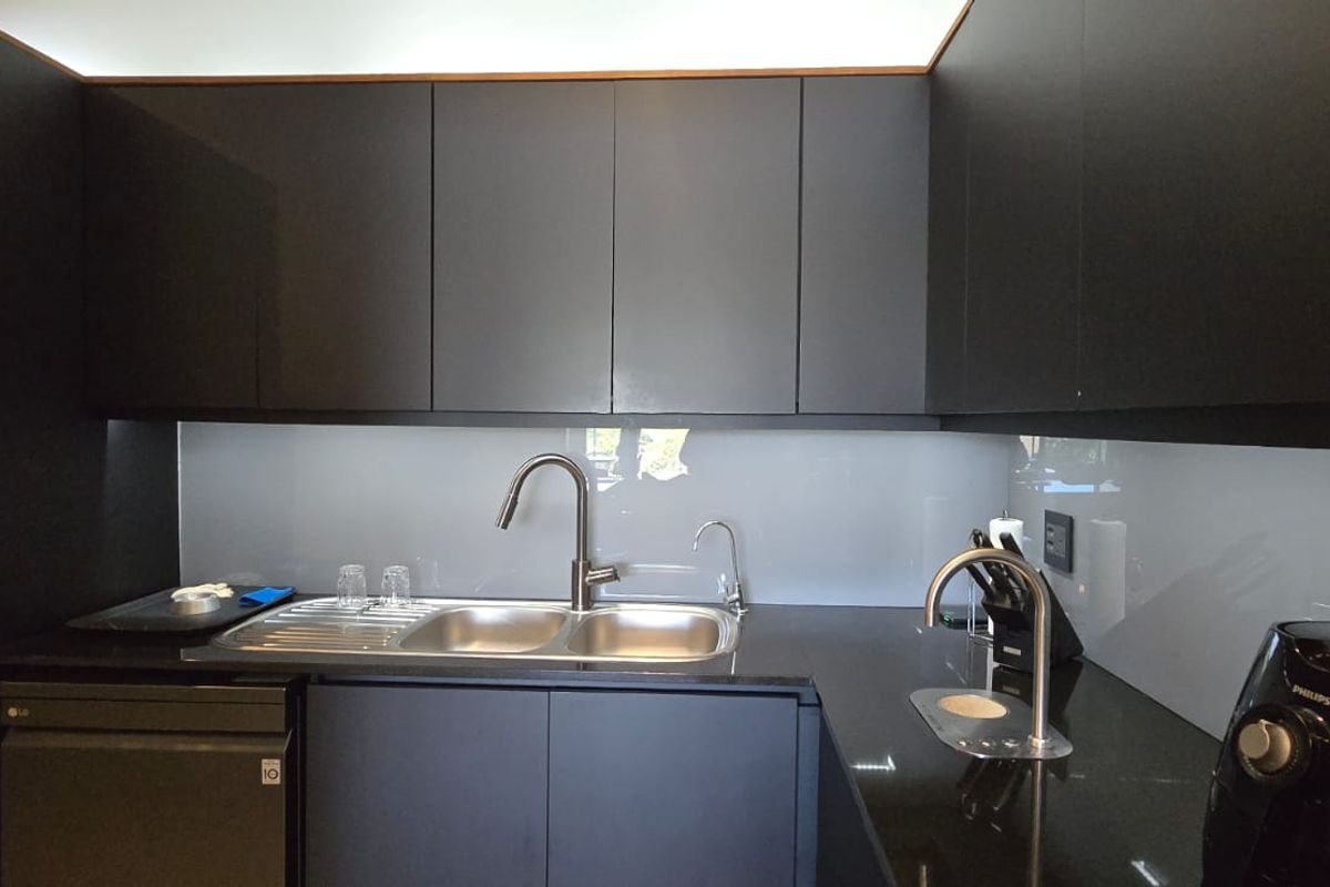 Modern kitchen featuring sleek matte black cabinetry, black granite countertops, a glass splashback, and integrated laundry facilities with high-quality fixtures.