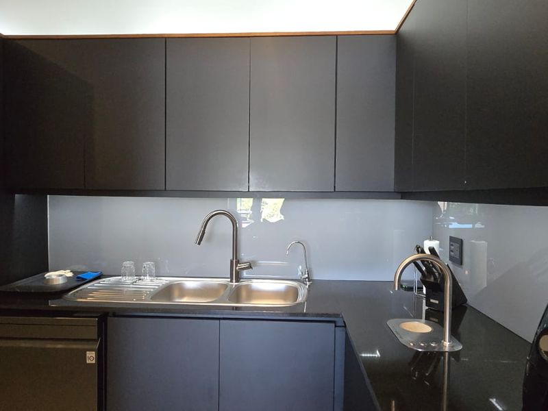 Modern kitchen featuring sleek matte black cabinetry, black granite countertops, a glass splashback, and integrated laundry facilities with high-quality fixtures.