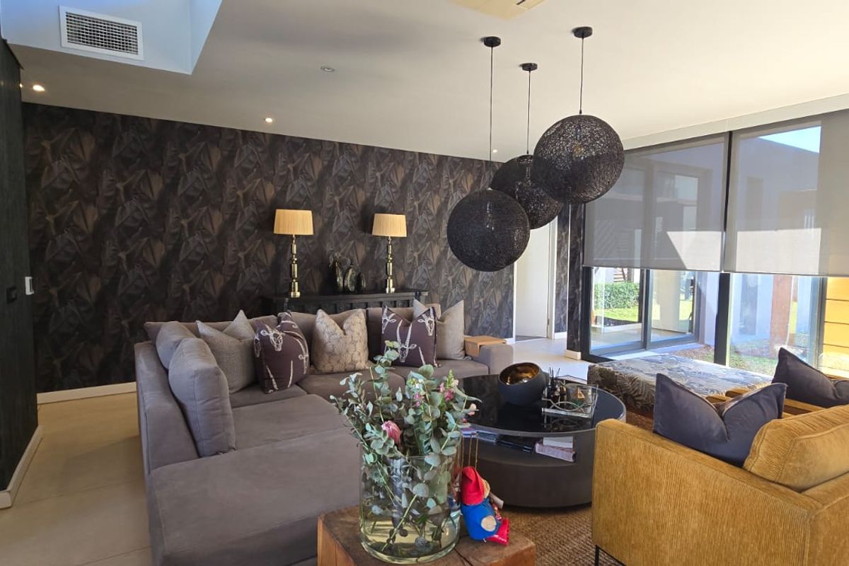 A modern, well-appointed living room featuring dark patterned wallpaper, large sliding glass doors with roller blinds, and recessed ceiling lighting.