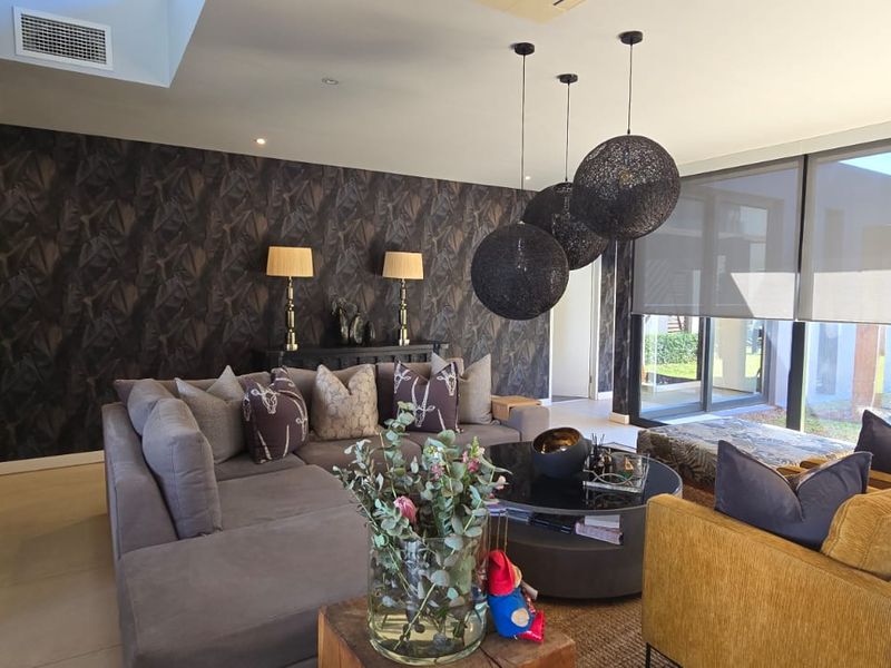 A modern, well-appointed living room featuring dark patterned wallpaper, large sliding glass doors with roller blinds, and recessed ceiling lighting.
